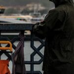 Žvejys su lietpalčiu žvejoja lietingą dieną