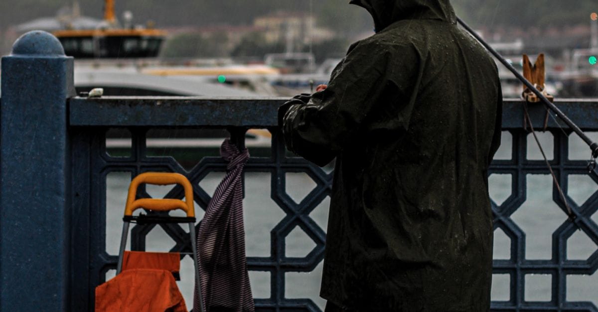 Žvejys su lietpalčiu žvejoja lietingą dieną